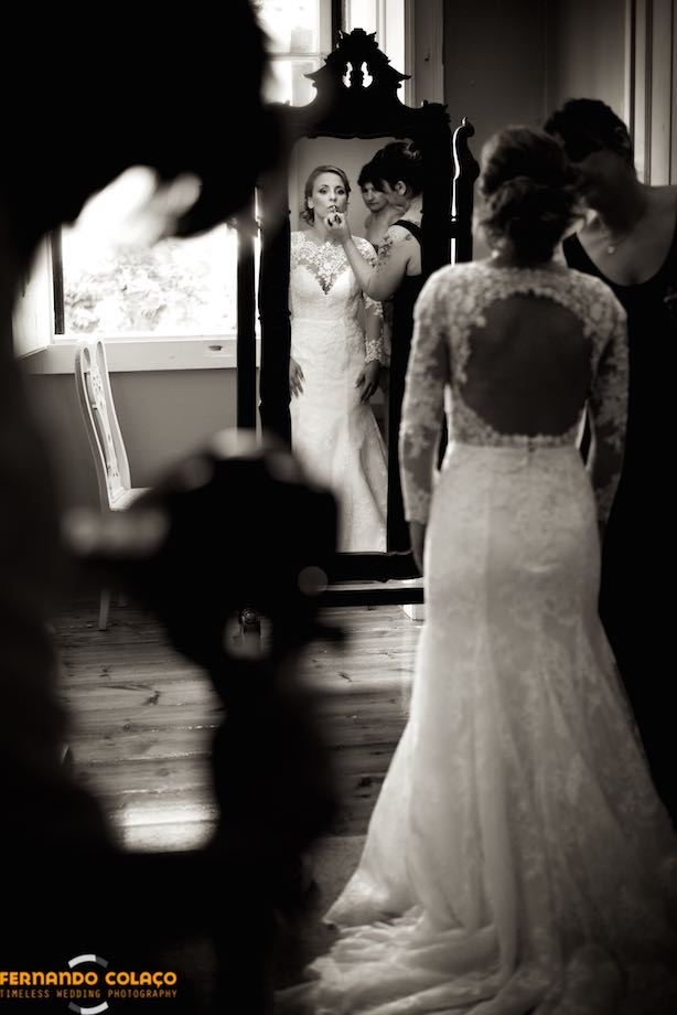 A maquilhadora pinta os lábios da noiva, reflectida num espelho grande na sala.