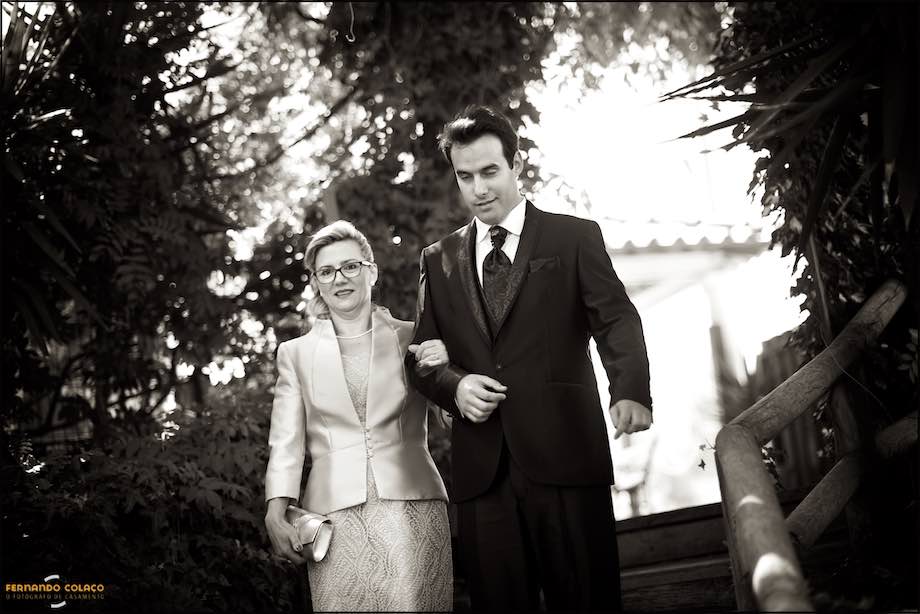 O noivo, de braço dado com a mãe, desce as escadas que o levam à mesa da cerimónia.