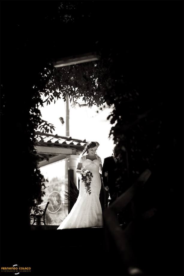 Por entre as plantas que dão acesso ao local da cerimónia do casamento, a noiva aparece de braço dado com o pai.