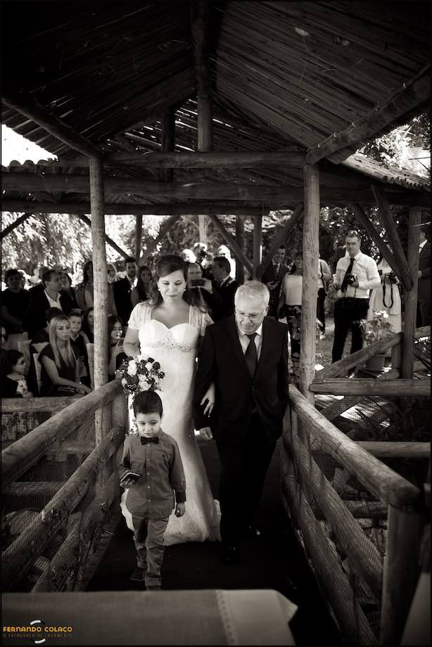 A noiva, com o pai e o menino das alianças, caminha no levadiço em madeira que leva à mesa cerimonial.