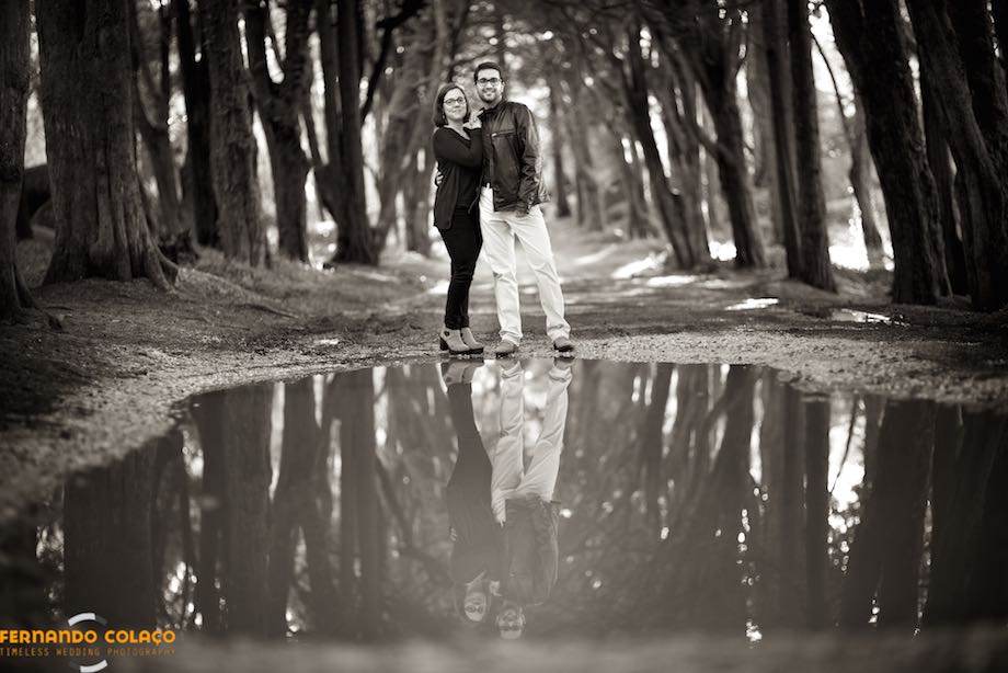 Numa estrada rodeada de árvores na Peninha em Sintra, o casal em frente de uma grande poça de água, com o seu reflexo, numa composição do fotógrafo de casamento.