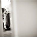 O noivo abotoa os sapatos enquanto se prepara para o casamento, visto numa abertura de uma porta pelo fotógrafo de casamento em Lisboa.