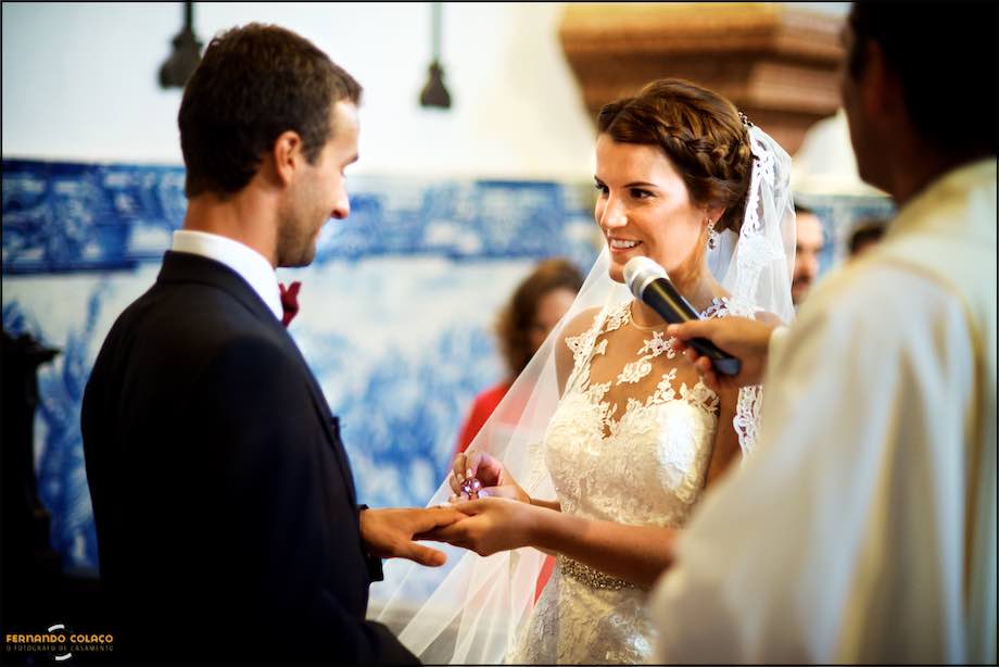 A noiva coloca a aliança no dedo do noivo na cerimónia, vista pelo fotógrafo de casamento em Leiria.