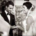 O noivo, em frente à noiva, quando lhe entrega a aliança no dedo na cerimónia, pelo fotógrafo de casamento.