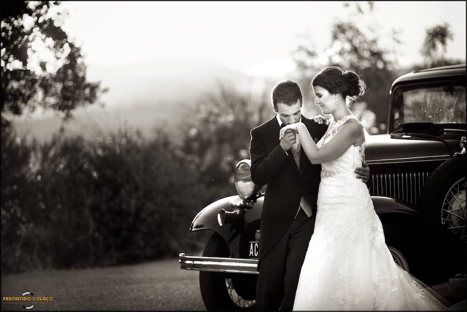 O noivo beija a mão da noiva, junto de um automóvel antigo, no jardim da Casa de Reguengos onde tem lugar a festa do casamento.