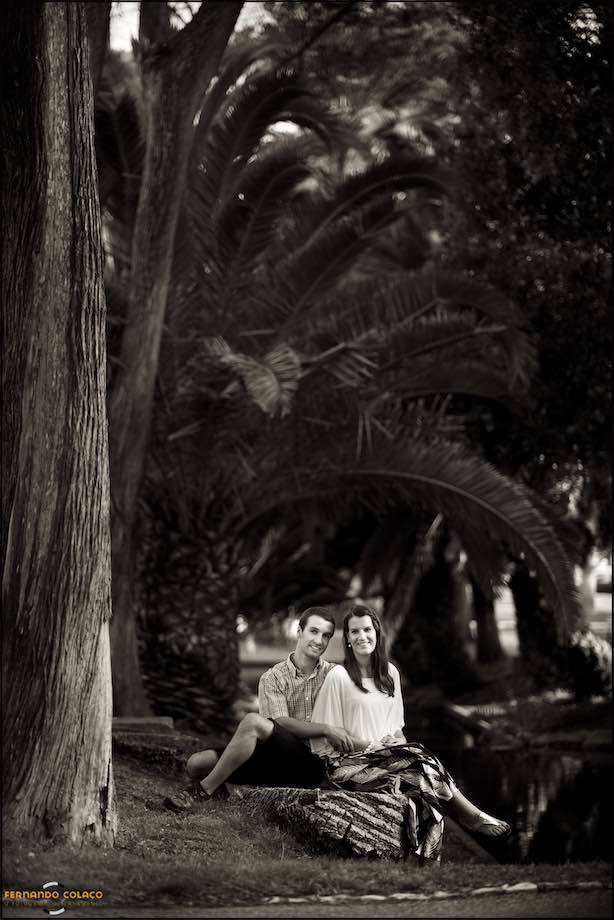 Junto do lago do Jardim do Casino do Estoril e debaixo das árvores antigas e frondosas, o casal, sentado e olhando em frente, posam para o fotógrafo de casamento.