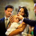 Menina bebé, no baptismo, na benção dos óleos pelo padrinho, vistos pelo fotógrafo de casamento em Lisboa.