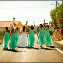 Antes da partida para a cerimónia, a noiva com as damas de honor festejam, de costas, na estrada com os seus ramos nas mãos ao alto, captadas pelo fotógrafo de casamento.
