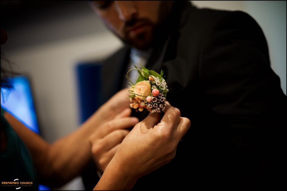 Mãos a colocar a flor de lapela no casaco do noivo, vistas pelo fotógrafo de casamento em Lisboa.