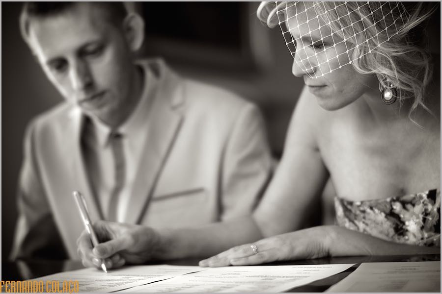 Noiva assina o documento do casamento junto do noivo, desfocado, vista pelo fotografo de casamento em Lisboa.
