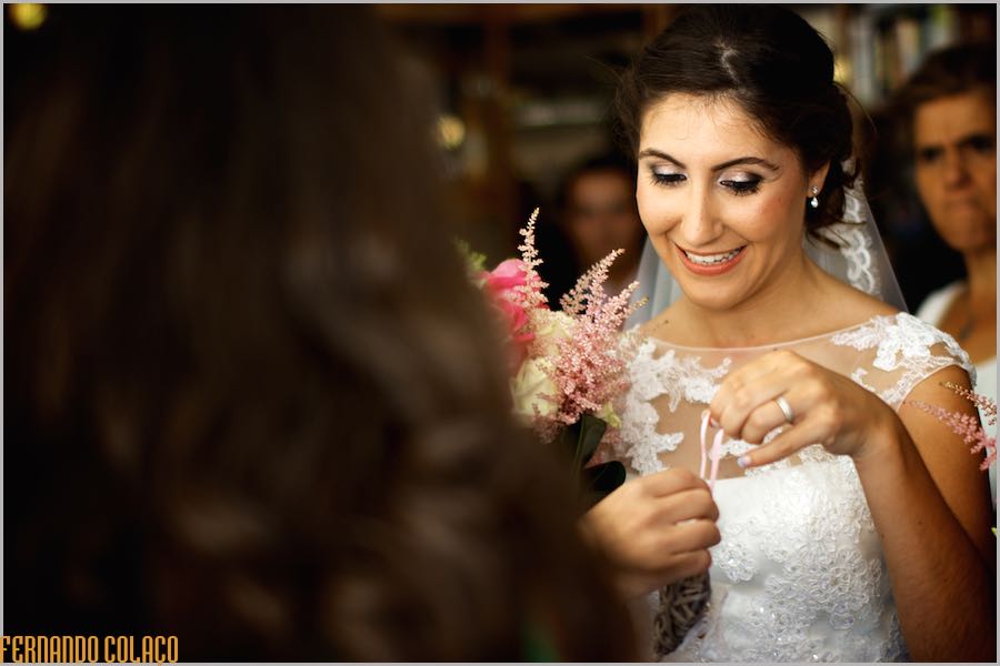 A noiva, sorrindo, recebe de alguém o coração de vime com as alianças do casamento, vista pelo fotógrafo de casamento.
