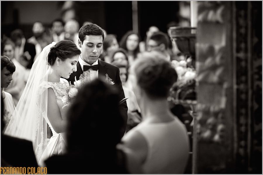 No meio dos convidados durante a cerimónia do casamento, os noivos, juntos, numa parte da liturgia, conforme o fotógrafo de casamento os viu.
