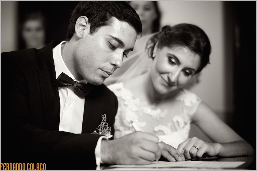 O noivo, ao lado da noiva, assina os documentos oficiais da igreja dando como finalizada a cerimónia de casamento.