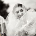 A noiva, envolta no véu do vestido de casamento, sorrindo de felicidade depois da cerimónia do casamento acabada, pelo fotógrafo de casamento.