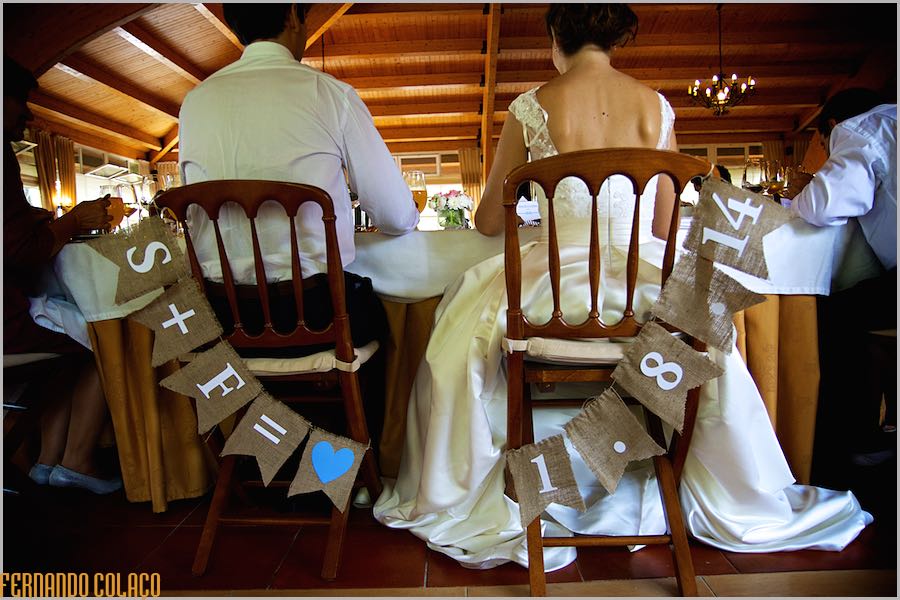 Os noivos vistos por detrás, sentados em cadeiras decoradas com o seu nome e a data do casamento, assim viu o fotógrafo de casamento.