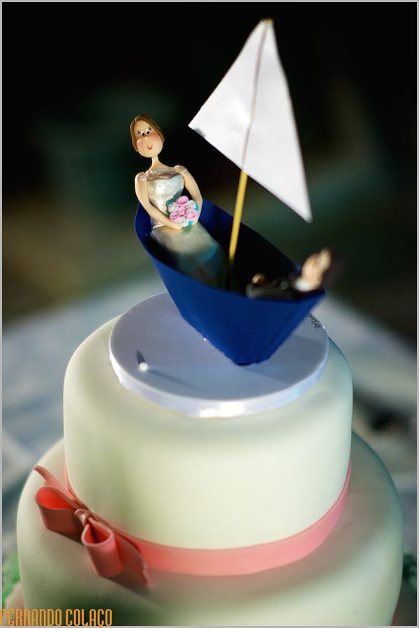 O bolo do casamento decorado com um barco à vela de papel, com noivos lá dentro, numa composição do fotógrafo de casamento.
