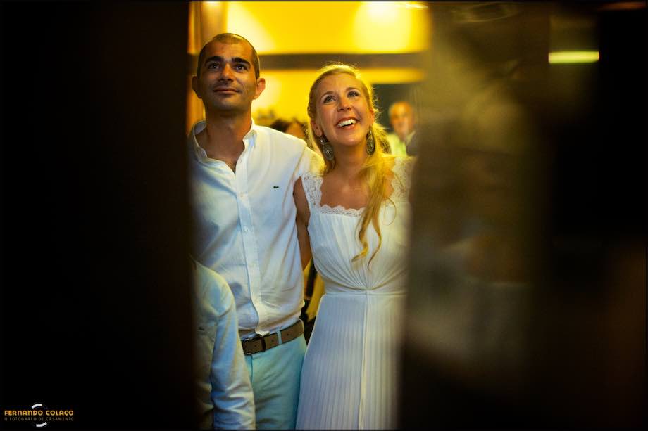 Os noivos riem do filme sobre eles, na festa no Club Nau em Ferragudo, by the wedding photographer in Algarve.