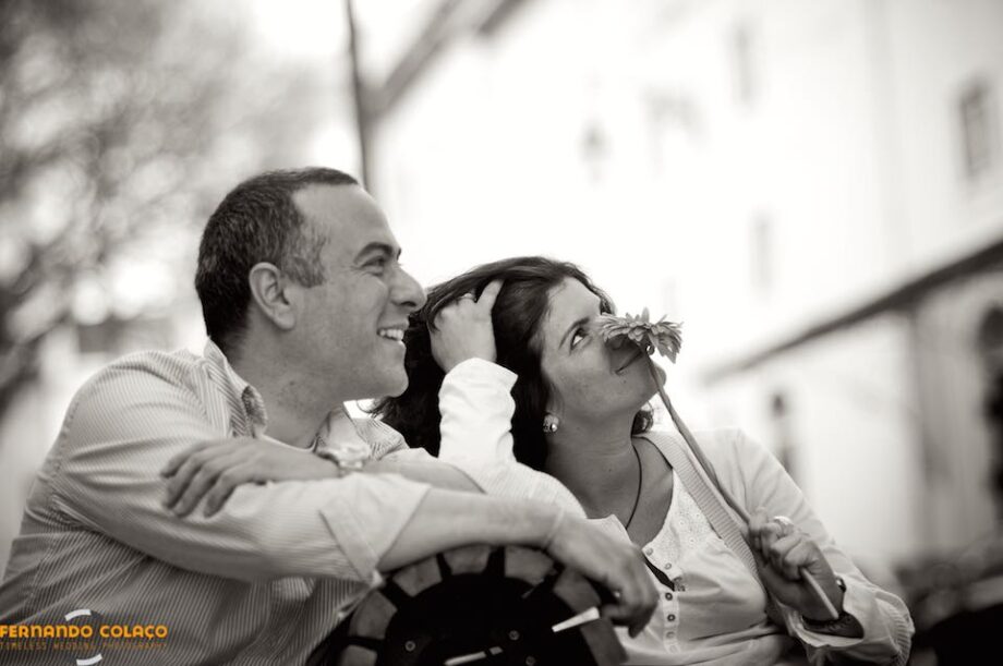 A noiva cheira uma flor com o noivo ao lado, olhando para cima, na sessão de pré casamento no Chiado, pelo fotógrafo de casamento em Lisboa.