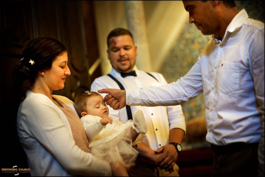 At the entrance to the Church for the christening ceremony, the bride's father in a ritual gesture of blessing, on the baby's face.