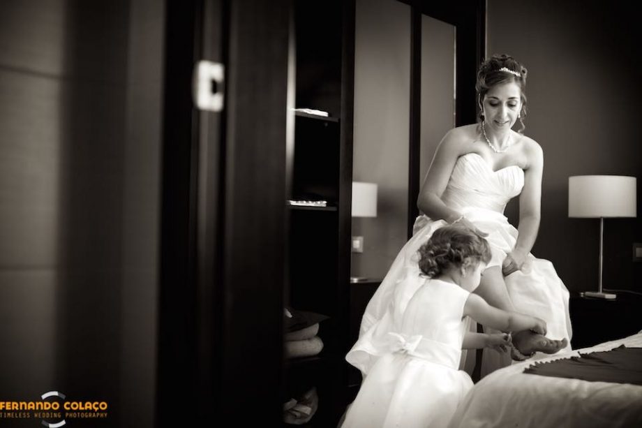 No fim da preparação da noiva para o casamento, a sua filha pequenina ajuda-a a pôr a liga na perna, pelo fotógrafo de casamento em Lisboa.