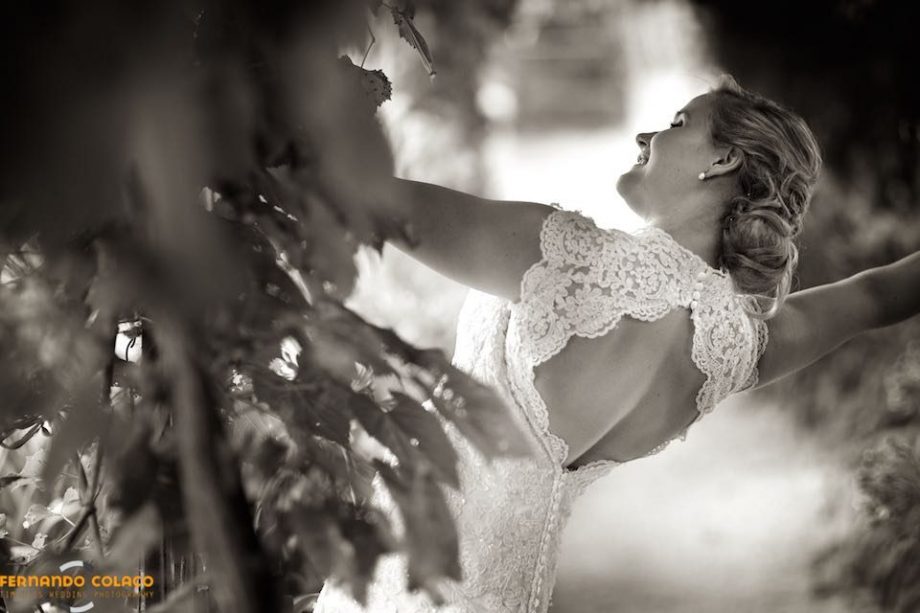 A noiva, com um sorriso feliz e de perfil, pendura-se na latada do jardim da  Quinta doa Alfinetes em Sintra.