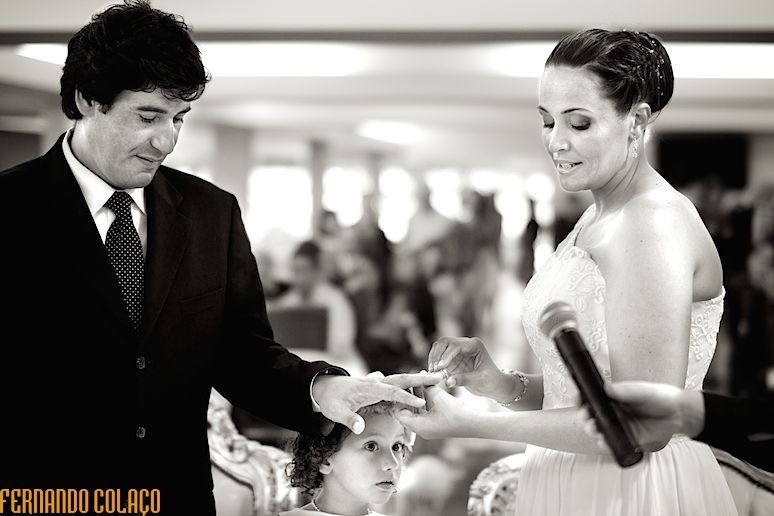 No momento da aliança no dedo do noivo, a sua filha vê por baixo das mãos dos noivos, durante a cerimónia do casamento na Quinta D. Nuno em Fátima, pelo fotógrafo de casamento..