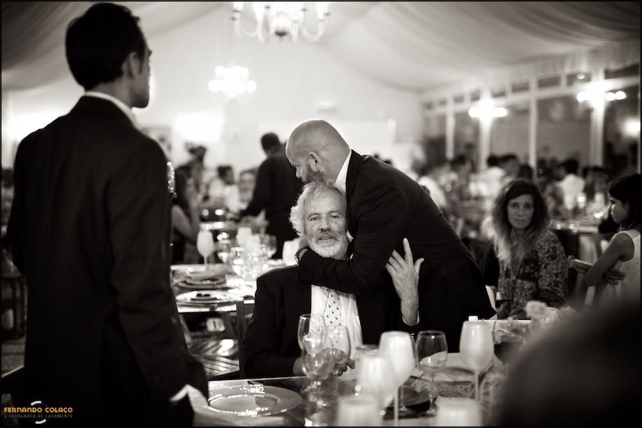 Um amigo, na festa do casamento na Quinta da Cascata, abraça outro, captados pelo fotógrafo de casamento.