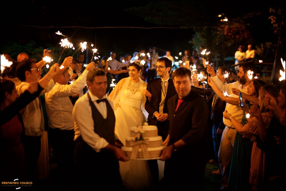 Bride and groom, very happy, illuminated by the lights that the guests wave, on their way to cutting the cake, in a view of the wedding photographer in Alentejo.