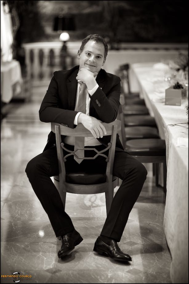 Black and white portrait of the groom sitting in the already empty wedding party room.