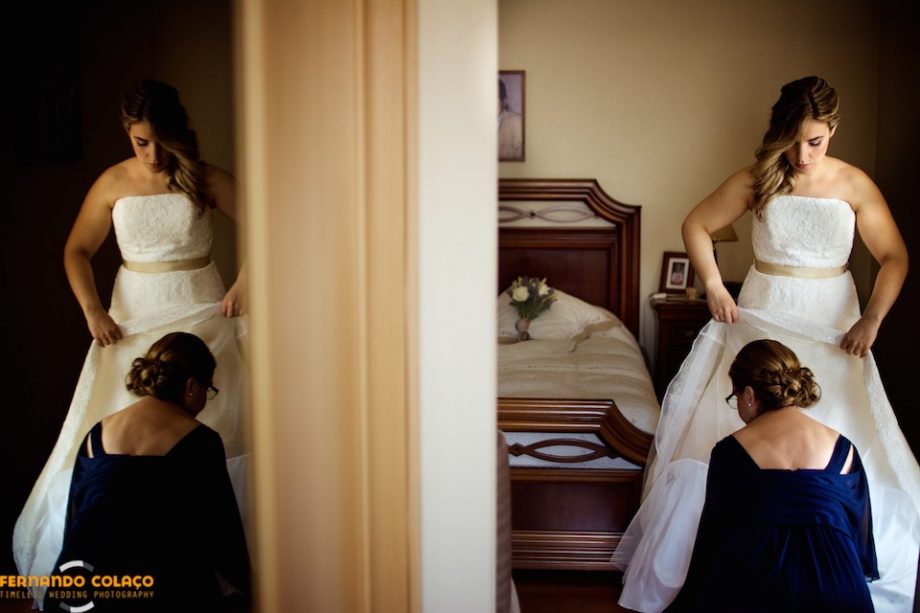 With a duplicated image in a mirror, the bride with her mother in the final adjustments of dressing the wedding dress, viewed by the Lisbon wedding photographer.
