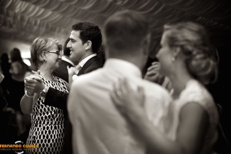 During the wedding party at Quinta dos Alfinetes in Sintra, the groom dances with the bride's mother, to be seen by her, out of focus, who dances with her father, by the wedding photographer in Sintra.