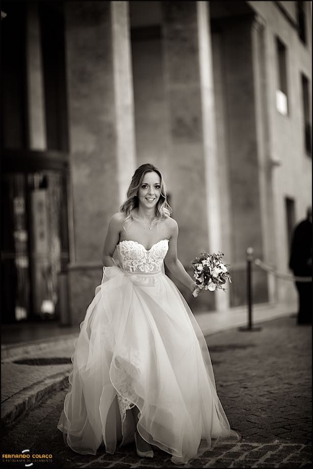 Noiva caminha pela rua com o bouquet na mão.