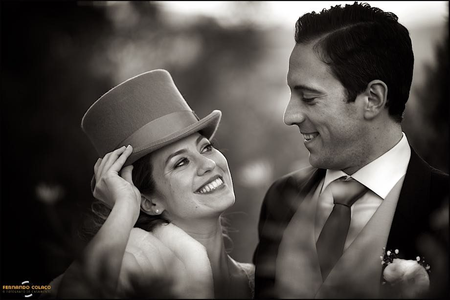 Fotografia a preto e branco de uma noiva com um chapéu junto no noivo, na sessão com o fotógrafo de casamento.