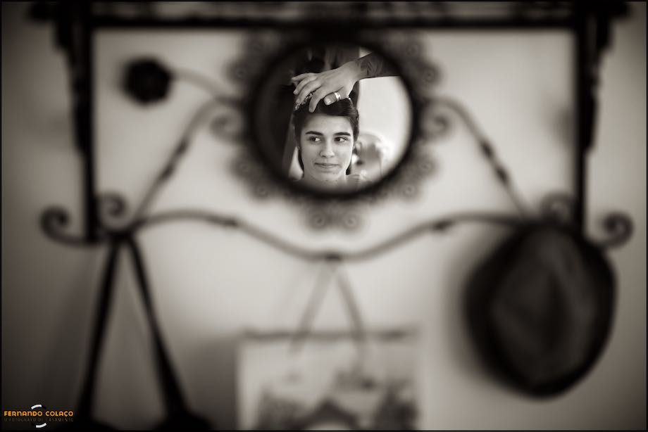 Mão da cabeleireira, sobre os cabelos da noiva, num espelho num cabide na casa do nos pais da noiva, pelo fotógrafo de casamento em Vila Real.