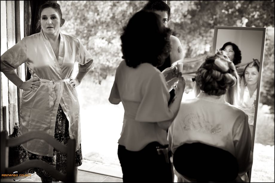 Noiva ao espelho rodeada da mãe, cabeleireira e uma amiga.
