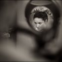 Cara da noiva, a preto e branco, num pequeno espelho de parede no cabeleireiro, no momento em que foi vista pelo fotógrafo de casamento.