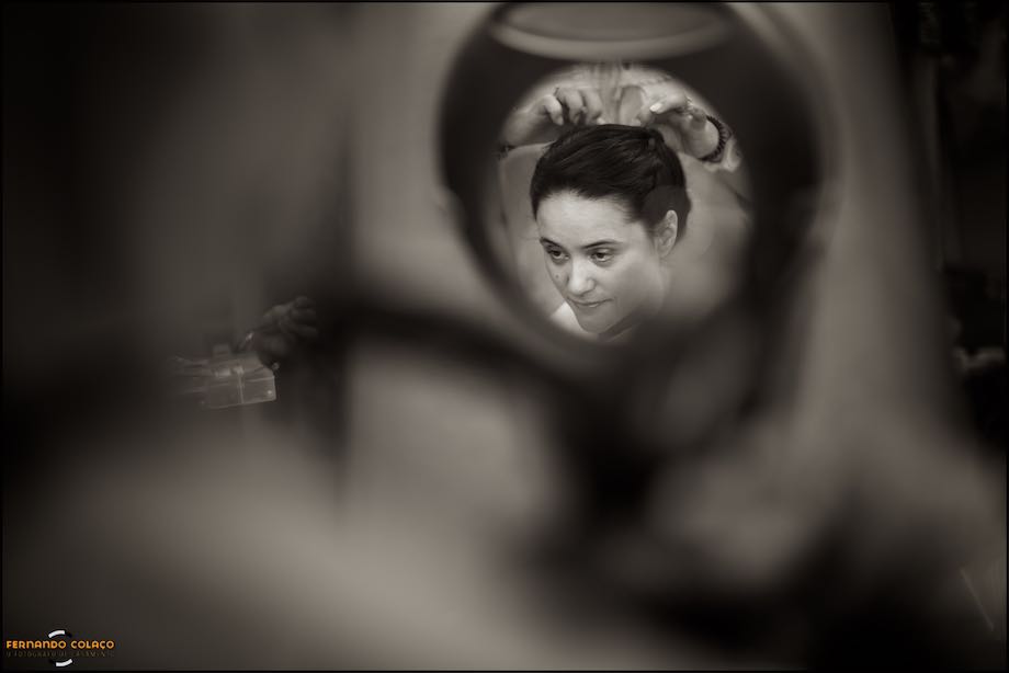 Cara da noiva, a preto e branco, num pequeno espelho de parede no cabeleireiro, no momento em que foi vista pelo fotógrafo de casamento.