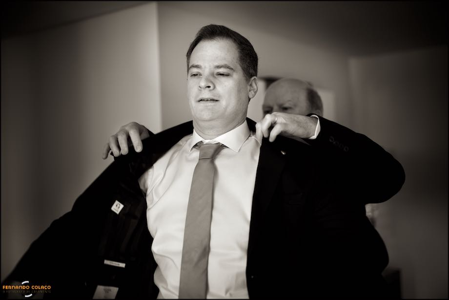 Mãos do pai noivo quando lhe veste o casaco, num momento pelo fotógrafo de casamento.