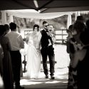 Noivos com o filho bebé, ao colo, saindo do local da cerimónia, no Club Nau, por entre os convidados, pelo fotógrafo de casamento no Algarve.