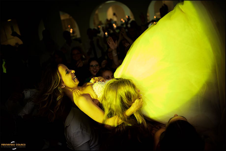 Noiva em ombros de convidados sob luz amarela, em festa de casamento na Quinta das Palmeira em Sintra.