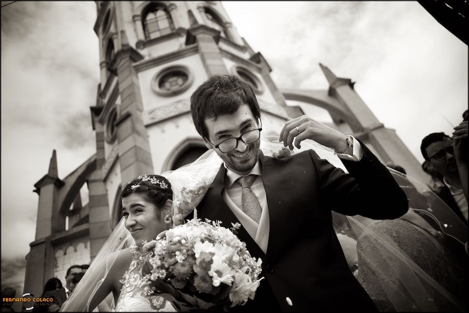 No final da saída da igreja, em fundo, o casal com ar feliz, num momento captado pelo fotógrafo de casamento.