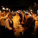 Noivos, muito felizes, iluminados pelas luzes que os convidados acenam, a caminho do corte do bolo, vistos pelo fotógrafo de casamento no Alentejo.
