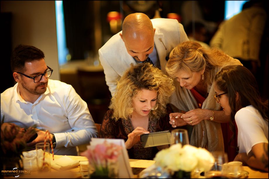 Cinco convidados olham atentamente para algo num telemóvel, num casamento no Palácio Estoril Golf & Wellness Hotel.