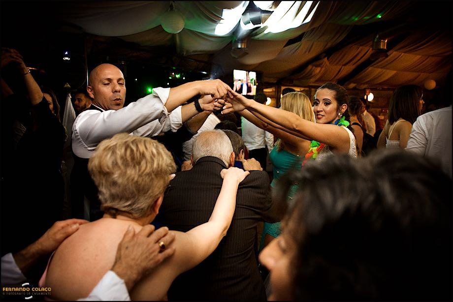 Os noivos fazem um arco com os braços para que outros passem por baixo, na festa do casamento, num momento visto pelo fotógrafo de casamento.