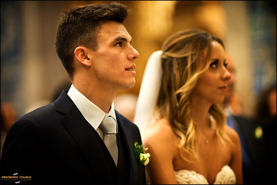 Noivo, olhando em frente, ao lado da noiva ouvindo o padre.