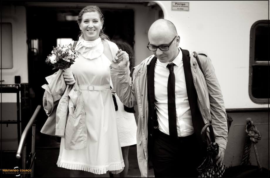 O noivo e a noiva, de mãos dadas, descem do barco na Trafaria.