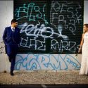 Casal fotografando em Lisboa em frente de porta d armazém cheia de escritos, com o fotógrafo de casamento.