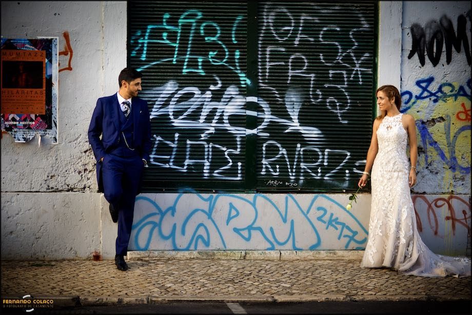 Casal fotografando em Lisboa em frente de porta d armazém cheia de escritos, com o fotógrafo de casamento.