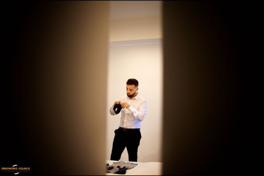 Through a half-open door, the groom is in the process of getting dressed for the wedding.