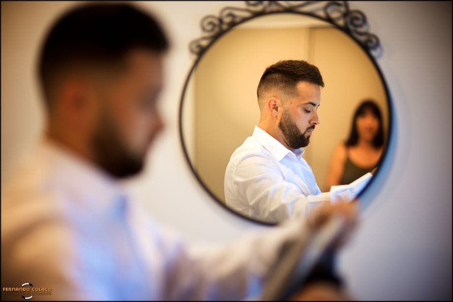 Groom in a round mirror with his mother blurred in the background.